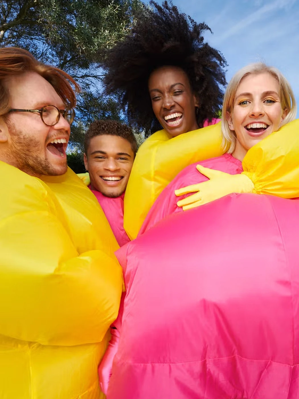 Campaign image: a group in yellow and pink inflatable suits, laughing together